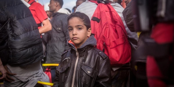 bambino che guarda dritto in camera mentre è circondato la persone 