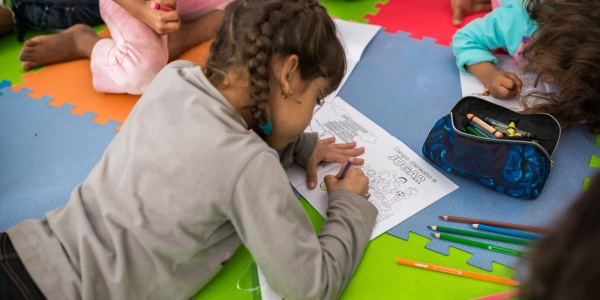 bambina sdraiata per terra su un tappeto colorato disegna