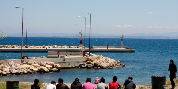 bambini migranti di spalle seduti davanti al mare