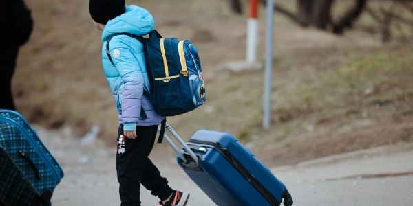 bambino vestito con vestiti invernali con trolley e zaino sulle spalle cammina per strada