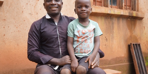 bambino mozambicano in braccio al suo papà fuori da una scuola