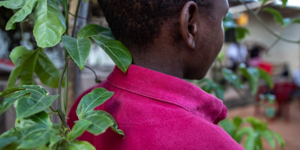 ragazzo di spalle davanti ad un albero che indossa un maglioncino fucsia