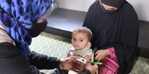 bambino siriano malnutrito in braccio alla madre mentre gli misurano il livello di malnutrizione tramite braccialetto MUAC