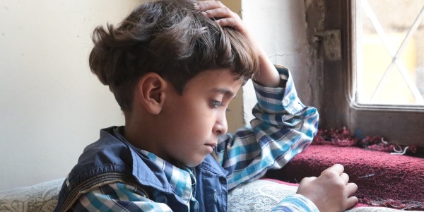 Bambino yemenita seduto di profilo vicino a una finestra guarda verso il basso