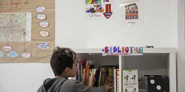 bambino con felpa grigia prende un libro da uno scaffale dedicato ai libri in unaula scolastica