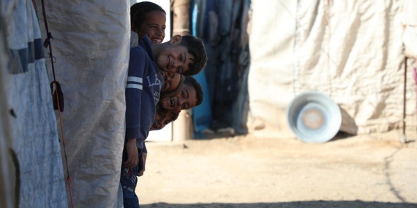 quattro bambini siriani sorridenti che spuntano fuori da una tenda Save the Children 