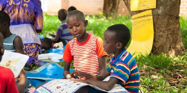 bambini seduti su un prato che leggono un cartellone con i numeri 