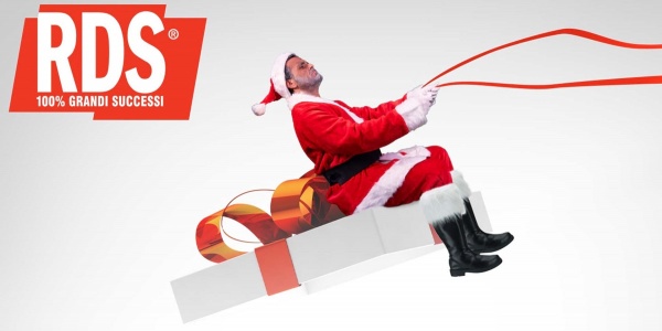Un uomo vestito da Babbo Natale è seduto sul coperchio di un pacco regalo che gli fa da slitta