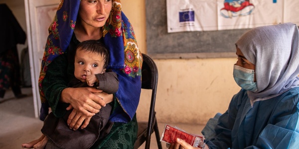 bambina in braccio a madre afghana mentre l'operatrice le offre assistenza sanitaria