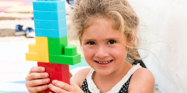 bambina sorridente con in mano una costruzione fatta di Lego colorati