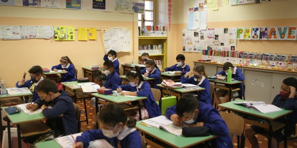 bambine e bambini sui banchi di scuola che scrivono su un foglio 