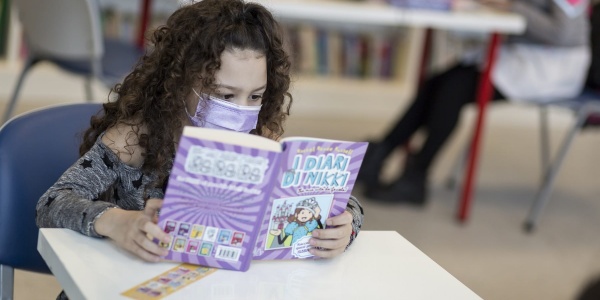 bambina mora con capelli ricci lunghi legge un libro seduta a una scrivania