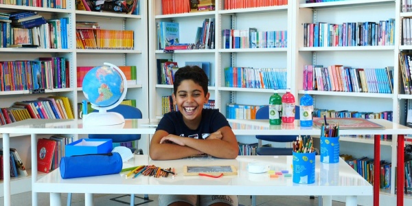 bambino seduto a scrivania con libri e penne sorride