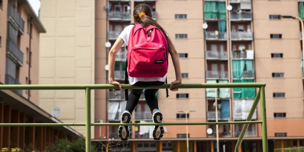 bambina seduta su una ringhiera verde davanti a dei palazzi