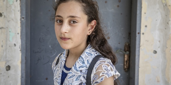 Mezzo busto di una bambina palestinese con fiocco bianco in testa e camicetta maniche corte bianca.