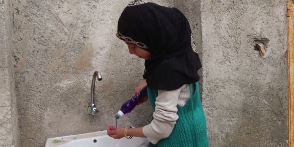 Bambina siriana di profilo vera il sapone sulle mani prima di lavarle al lavandino di fronte a lei.