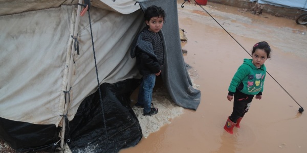 Due bambini siriani fuori alla loro tenda in un campo profughi stanno in piedi nel terreno allagato