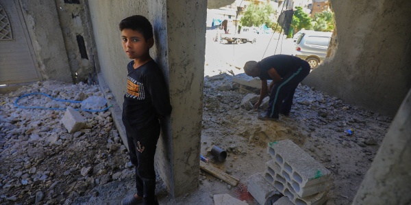 Un bambino è appoggiato con la schiena a un muro dentro un edificio distrutto e in mezzo alle macerie