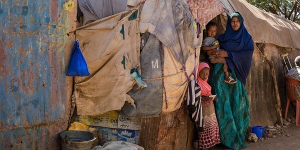 Madre con in braccio il proprio bambino e accanto alla figlia davanti alla loro capanna in Somalia