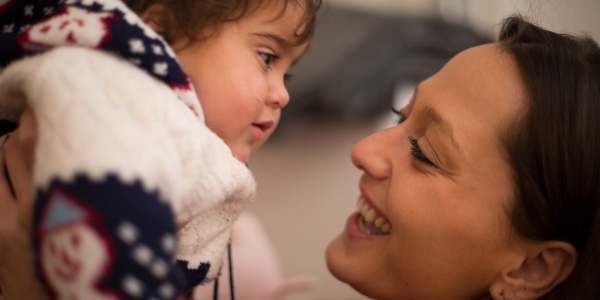 Primo piano di donna che guarda la bimba sollevata in braccio davanti lei.