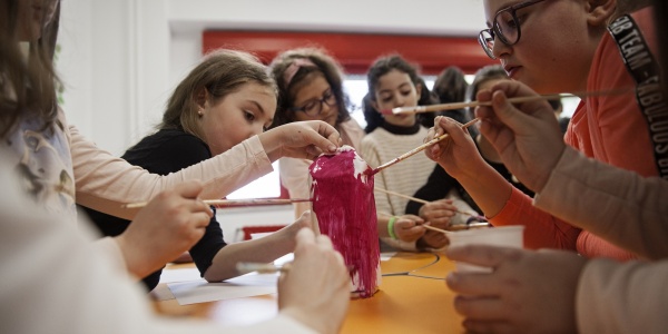 5 ragazze al banco di scuola stanno dipingendo di rosa un loro lavoro artistico