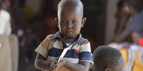 Mezzo busto di un bambino sudanese con maglietta a righe arancioni blu e bianche che tiene con due mani un foglio