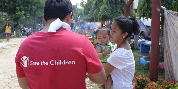Operatore Save the Children presta assistenza a una mamma filippina con bambino in braccio