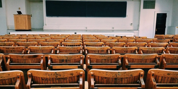 Aula universitaria vuota con sedie di legno pieghevoli, lavagna e leggio su un rialzo.