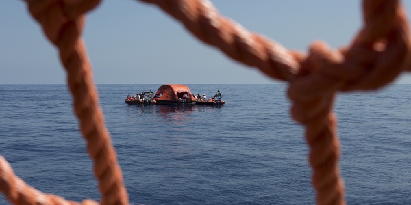 primo piano di una rete rossa di una barca dalla quale si vede il mare e un barchino di salvataggio a pochi metri