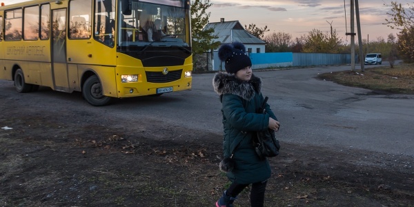 bambina cammina di fronte ad uno scuola bus giallo in Ucraina