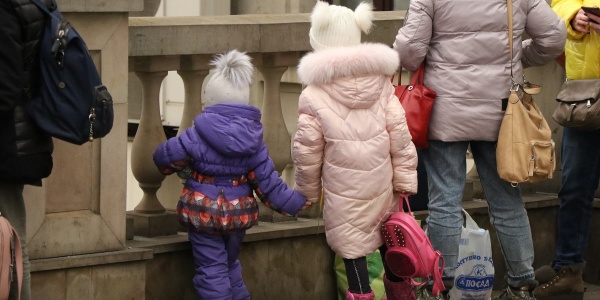 Due bambine di spalle con i giacconi si danno la mano e guardano avanti affacciate a una balaustra.