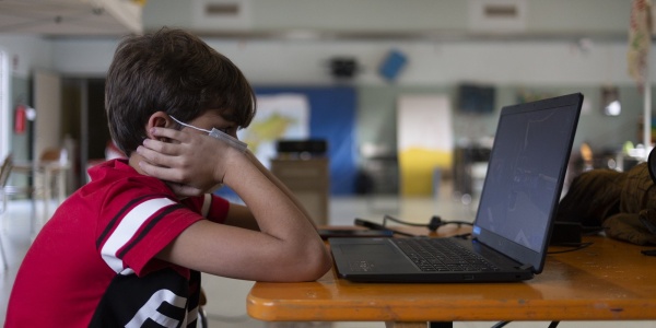 bambino seduto davanti al PC indossa una mascherina per proteggersi dal covid-19