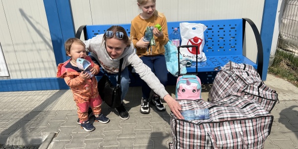mamma con due bimbi su una panchina blu con logo save the children italia con una busta con aiuti umanitari