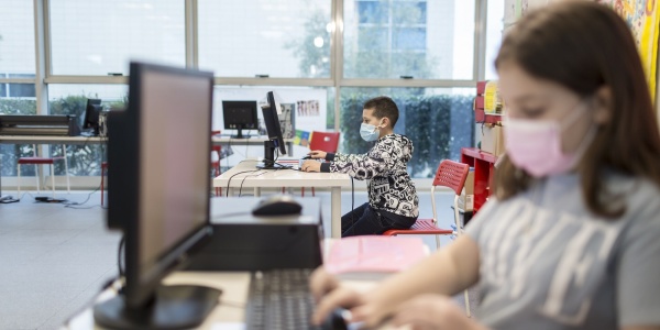 bambina in primo piano e bambino in secondo piano entrambi seduti alla scrivania mentre scrivono al PC