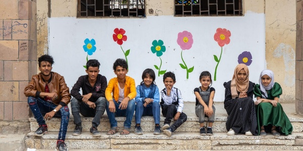 Bambini e ragazzi seduti in linea su scalini con dietro sul muro fiori dipinti da loro