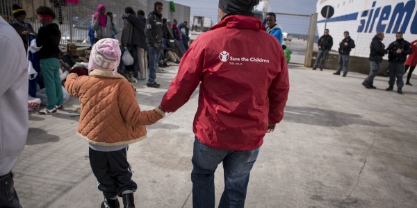 Operatore umanitario save the children mano nella mano con una bambina